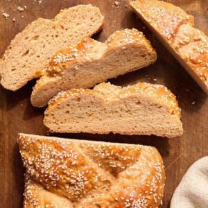 Gluten free challah bread sliced on a wooden board with sesame seeds showing the soft interior crumb.