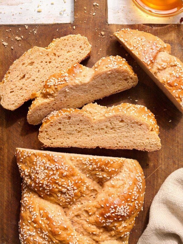 Gluten free challah bread sliced on a wooden board with sesame seeds showing the soft interior crumb.