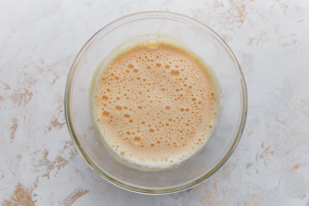 Egg yolks tempered with warm lemon mixture in a bowl to prepare the lemon custard filling