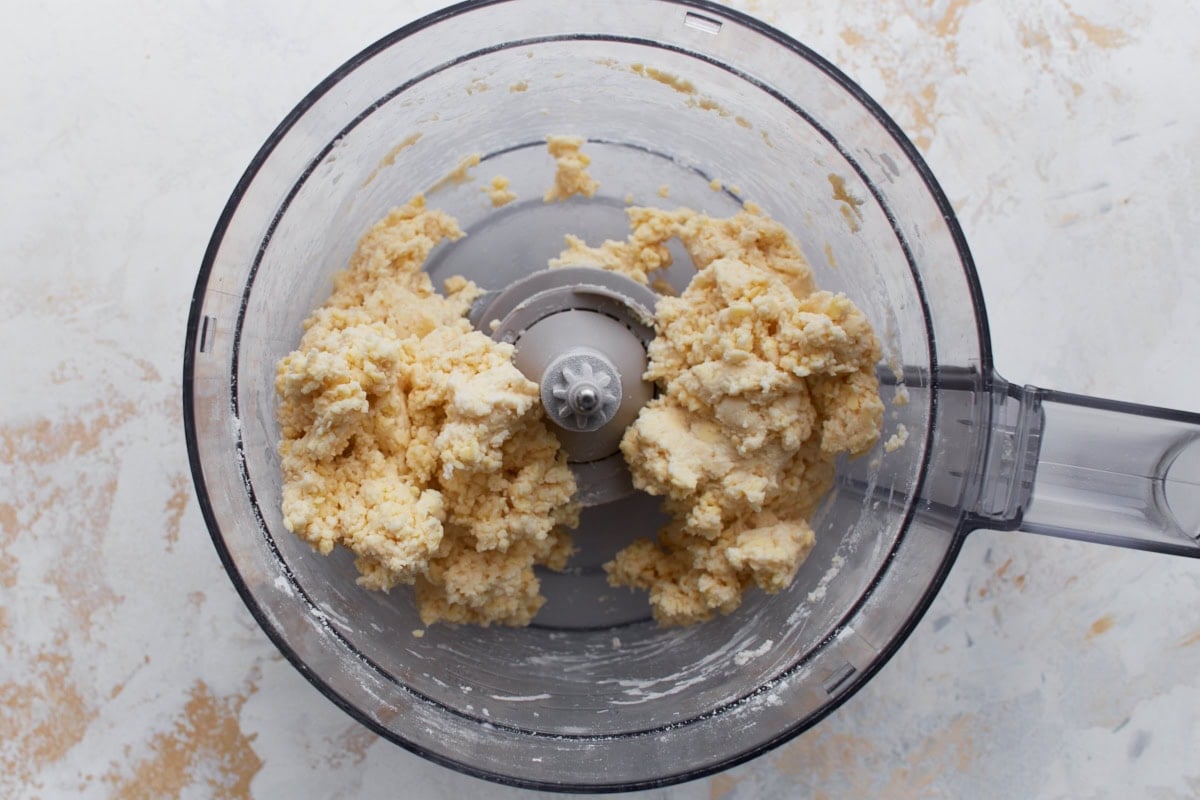 Gluten-free pie dough beginning to come together in a food processor after adding cold water