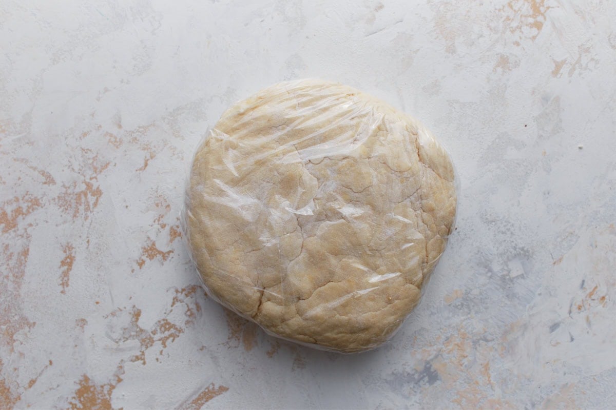 Gluten-free pie dough shaped into a disk and wrapped in plastic wrap before chilling