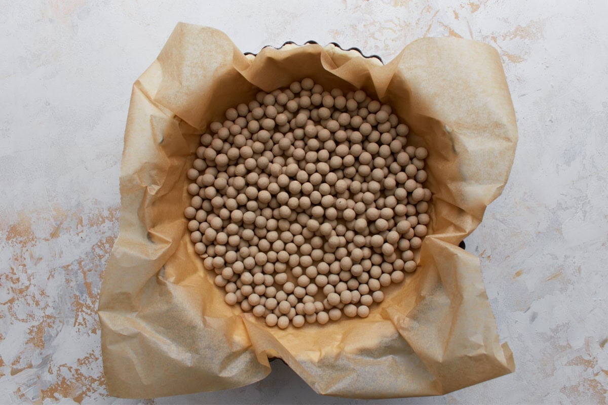 Gluten-free pie crust lined with parchment paper and filled with pie weights for blind baking