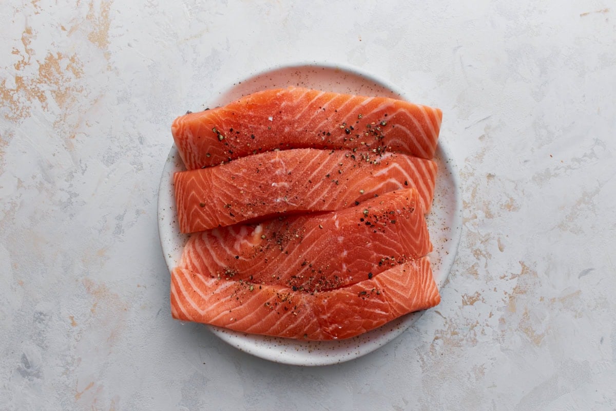 Raw salmon fillets seasoned with salt and black pepper on a white plate