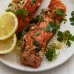 Keto salmon fillets with garlic butter sauce, fresh parsley, and lemon slices on a plate
