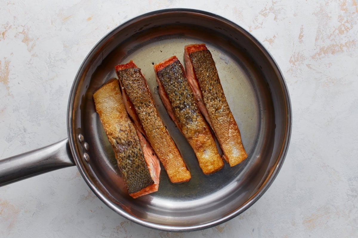 Salmon fillets cooking skin-side down in a skillet with crispy golden skin