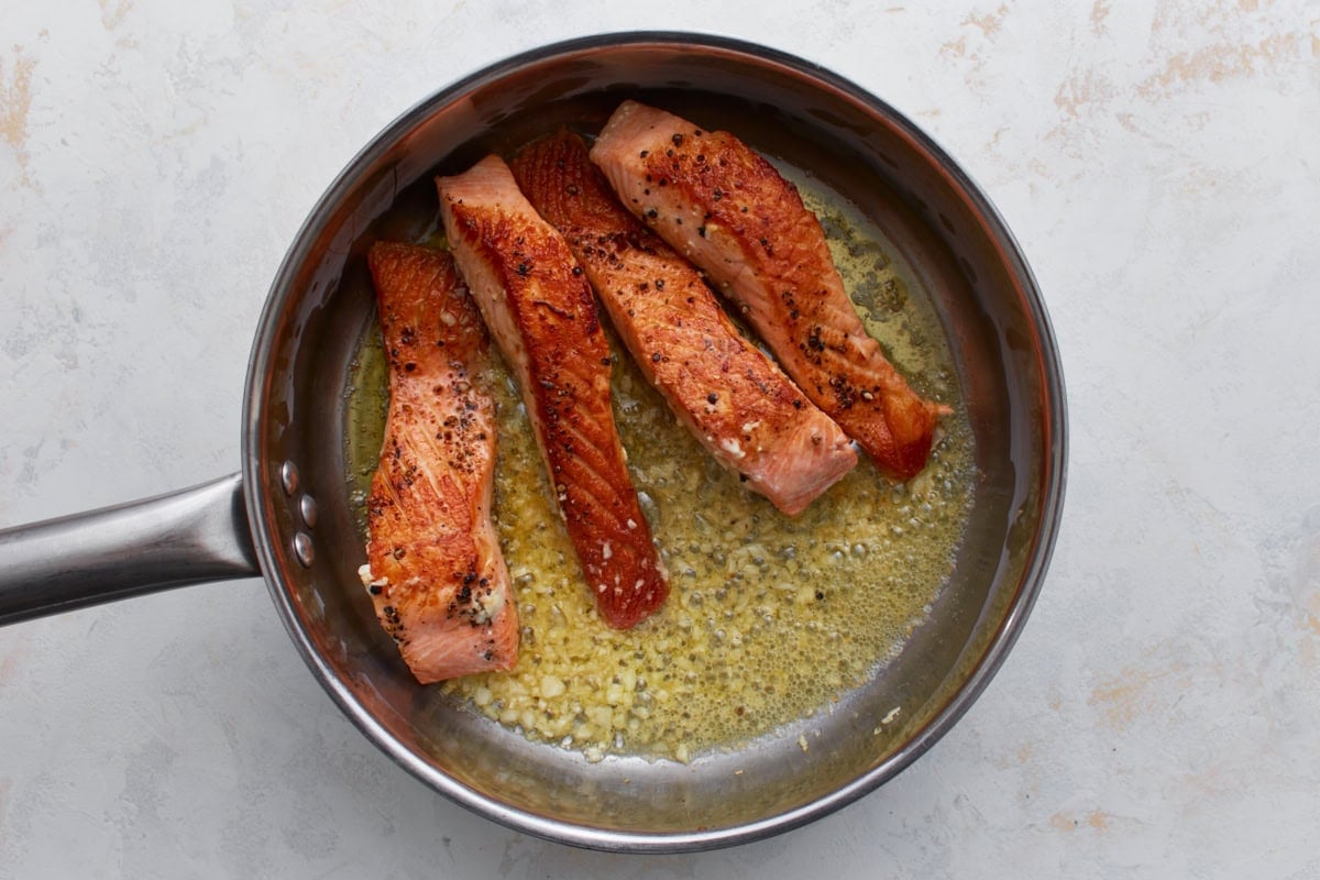 Seared salmon in a pan with melted butter and minced garlic