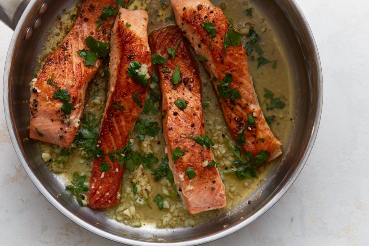 Keto salmon finished with garlic butter sauce and fresh parsley in skillet