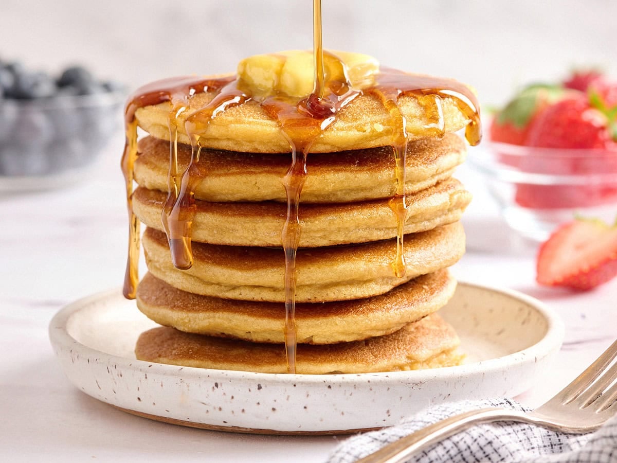 Stack of coconut flour pancakes with butter and syrup, one pancake cut to show soft fluffy interior