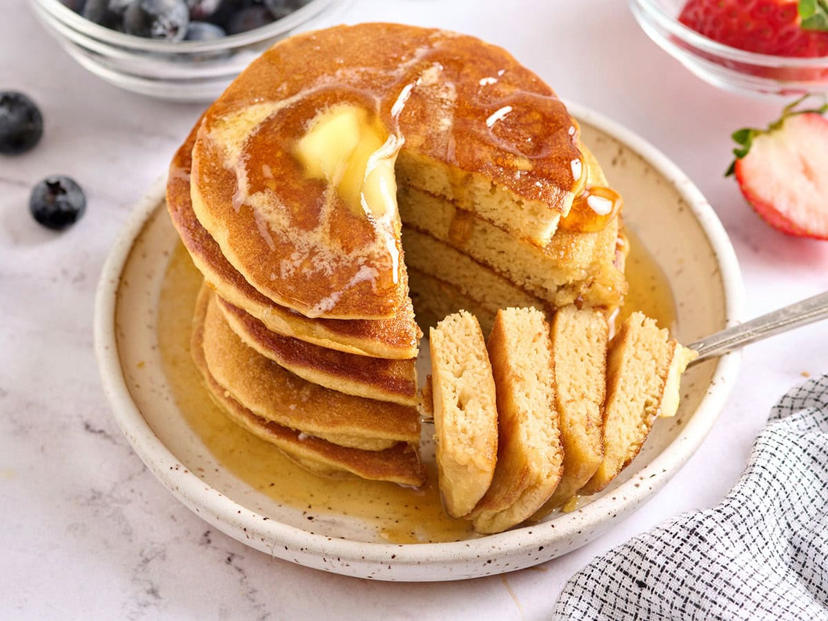 Stack of coconut flour pancakes with butter and maple syrup being poured over the top