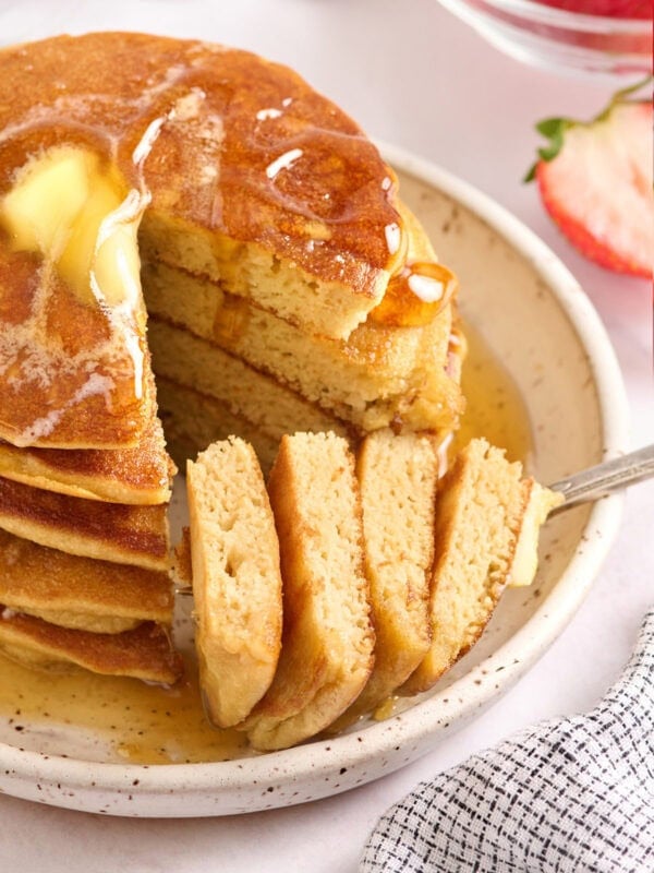 Stack of coconut flour pancakes with butter melting on top and maple syrup drizzled, showing a soft fluffy interior