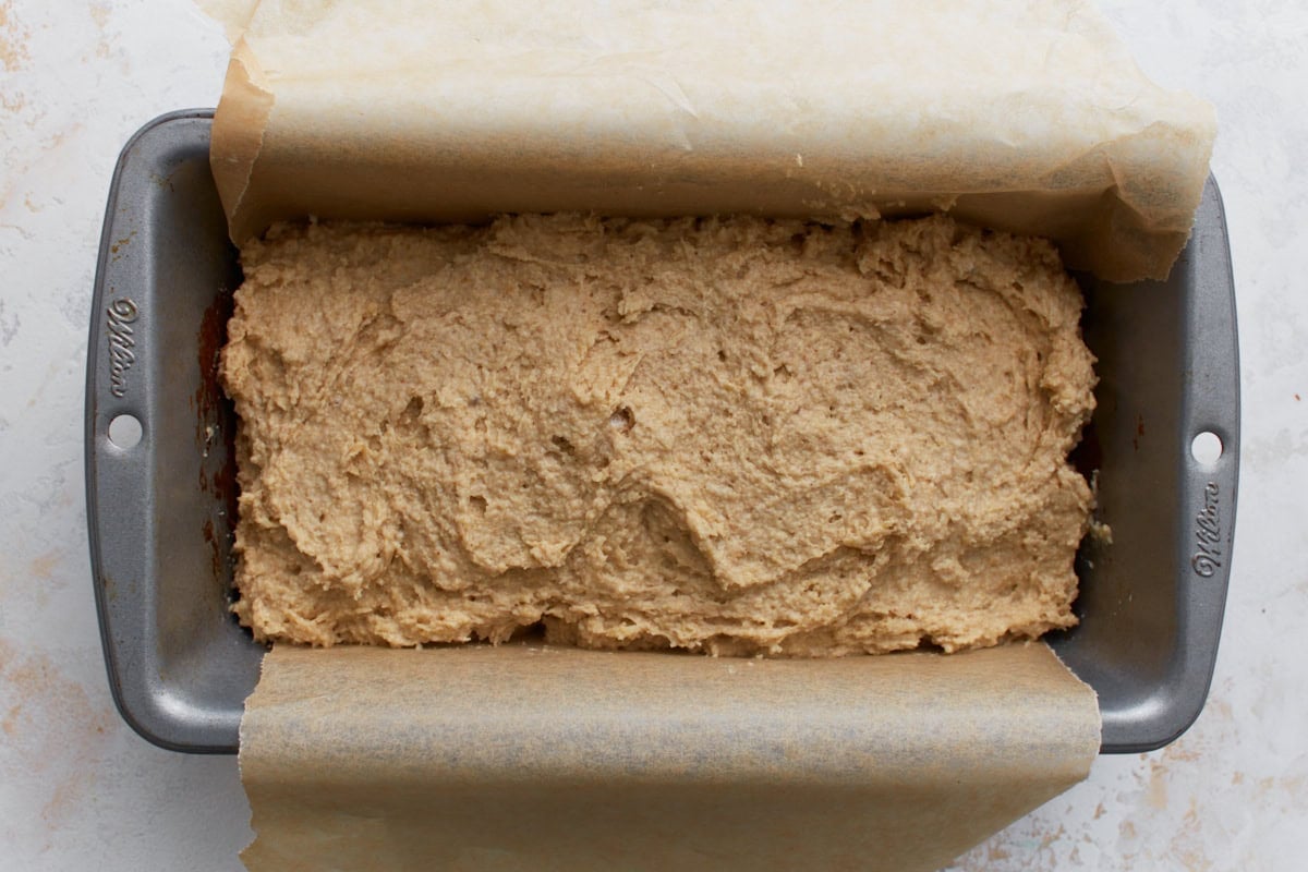 Oat flour bread batter spread into a parchment-lined loaf pan before baking