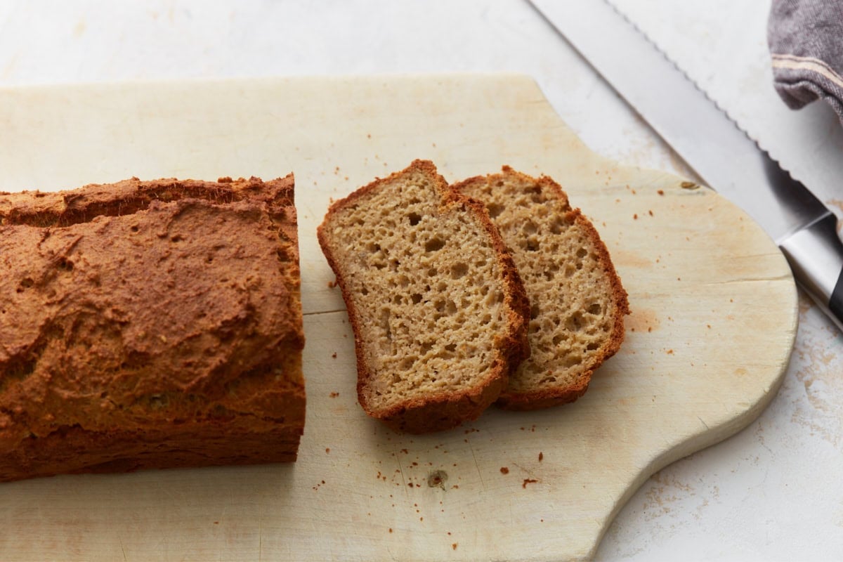 Oat flour bread loaf with two slices cut on a wooden cutting board with visible crumb texture