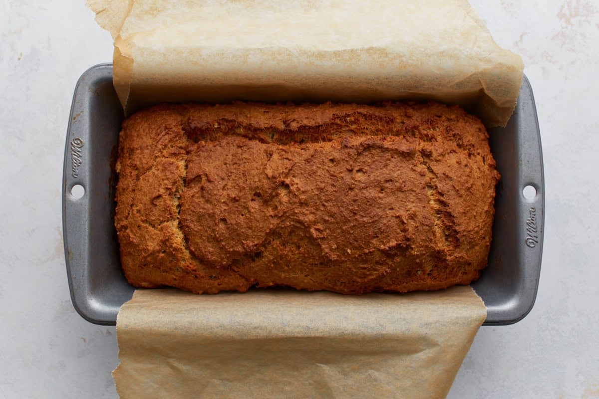Freshly baked oat flour bread in a loaf pan with golden crust and cracked top