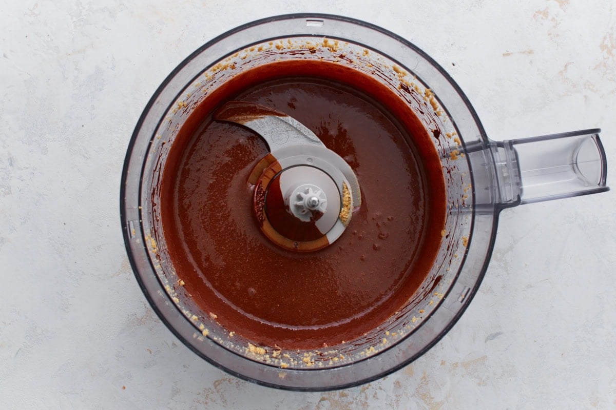 Chocolate hazelnut mixture in a food processor after adding melted chocolate, smooth and glossy