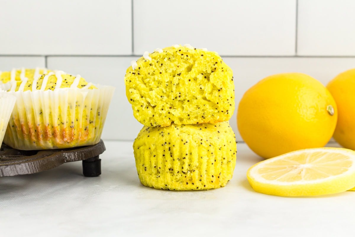 Gluten-free lemon poppy seed muffins stacked to show moist crumb and poppy seeds with fresh lemons in background
