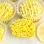 Gluten-free lemon poppy seed muffins with lemon glaze in white liners, one muffin sliced open to show moist crumb and poppy seeds
