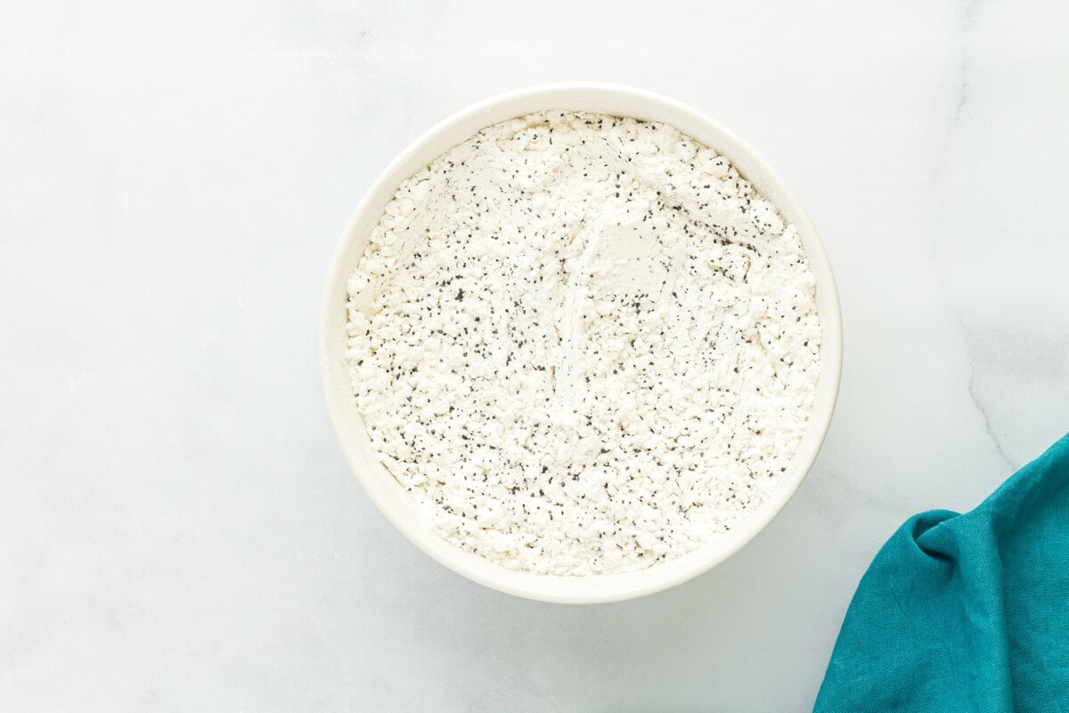 Gluten-free flour mixture with poppy seeds in a white bowl on marble surface
