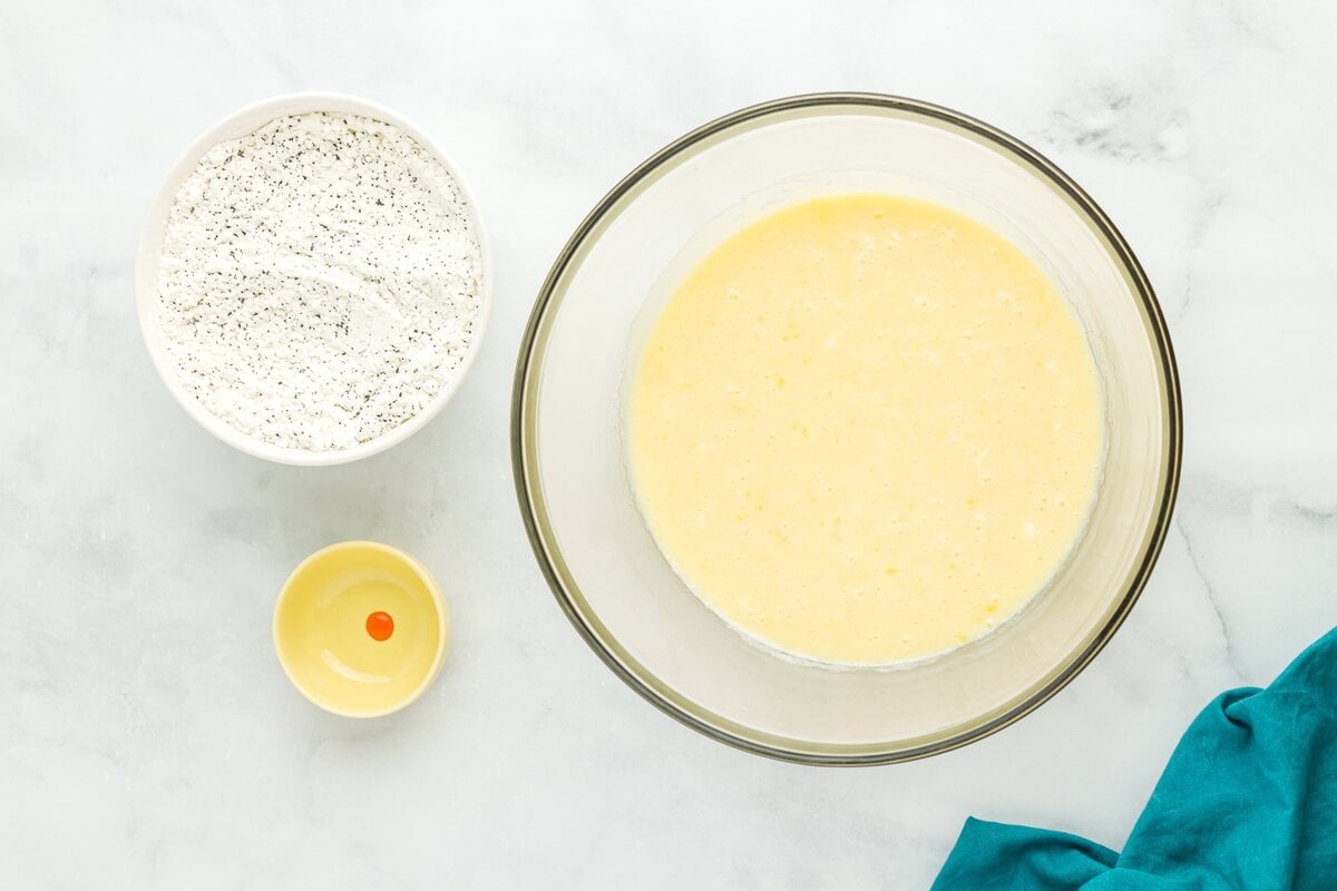 Wet ingredients for gluten-free lemon poppy seed muffins mixed in a large glass bowl with small bowl of food coloring beside it