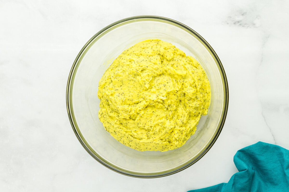 Thick gluten-free lemon poppy seed muffin batter in glass mixing bowl showing bright yellow color and poppy seeds