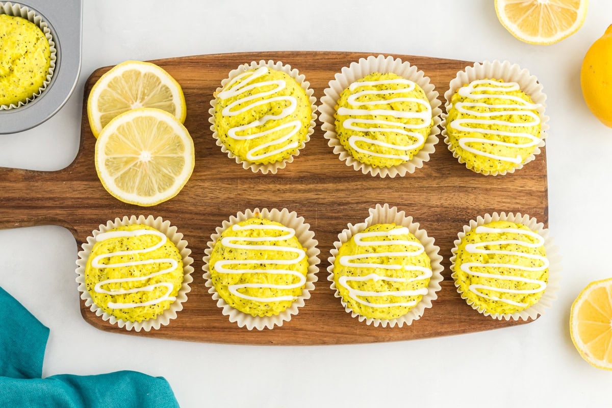 Gluten-free lemon poppy seed muffins with white lemon glaze on wooden board with fresh lemon slices
