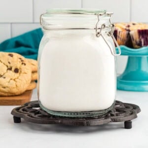 Homemade gluten free flour blend stored in an airtight glass jar with cookies and muffins in the background