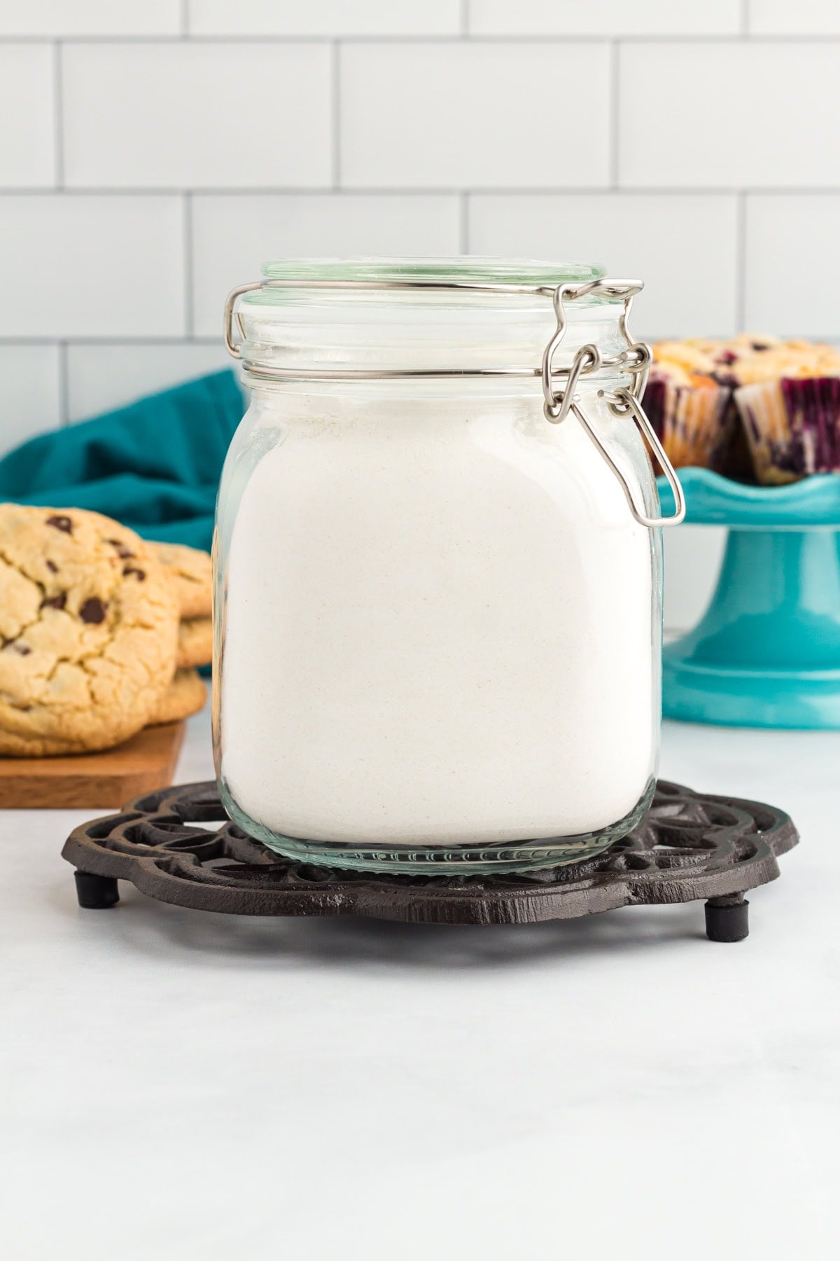 Homemade gluten free flour blend stored in an airtight glass jar with cookies and muffins in the background