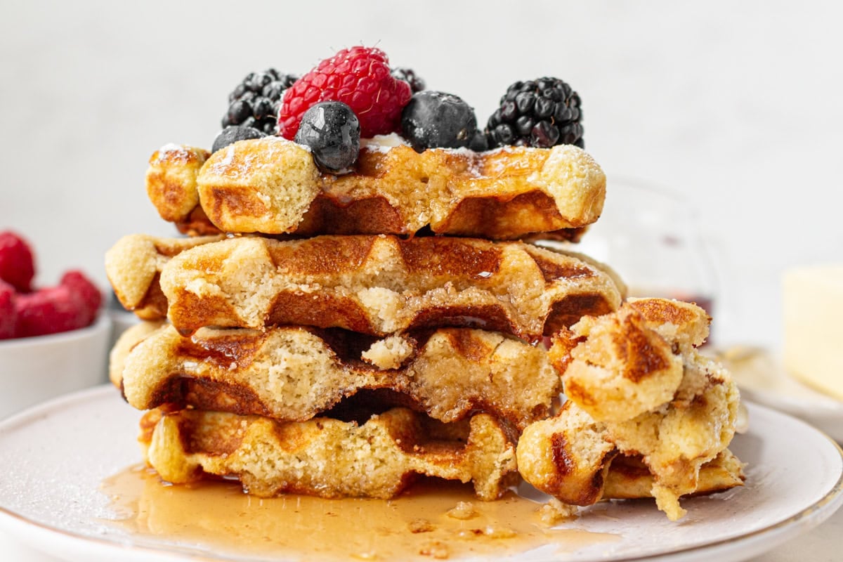 Stack of gluten-free coconut flour waffles topped with fresh berries and maple syrup showing soft interior texture