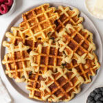 Plate of golden brown gluten-free coconut flour waffles served with fresh berries, butter, and maple syrup