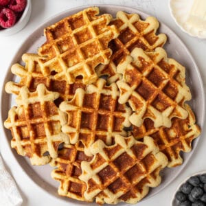 Plate of golden brown gluten-free coconut flour waffles served with fresh berries, butter, and maple syrup