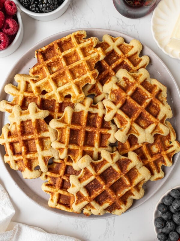 Plate of golden brown gluten-free coconut flour waffles served with fresh berries, butter, and maple syrup