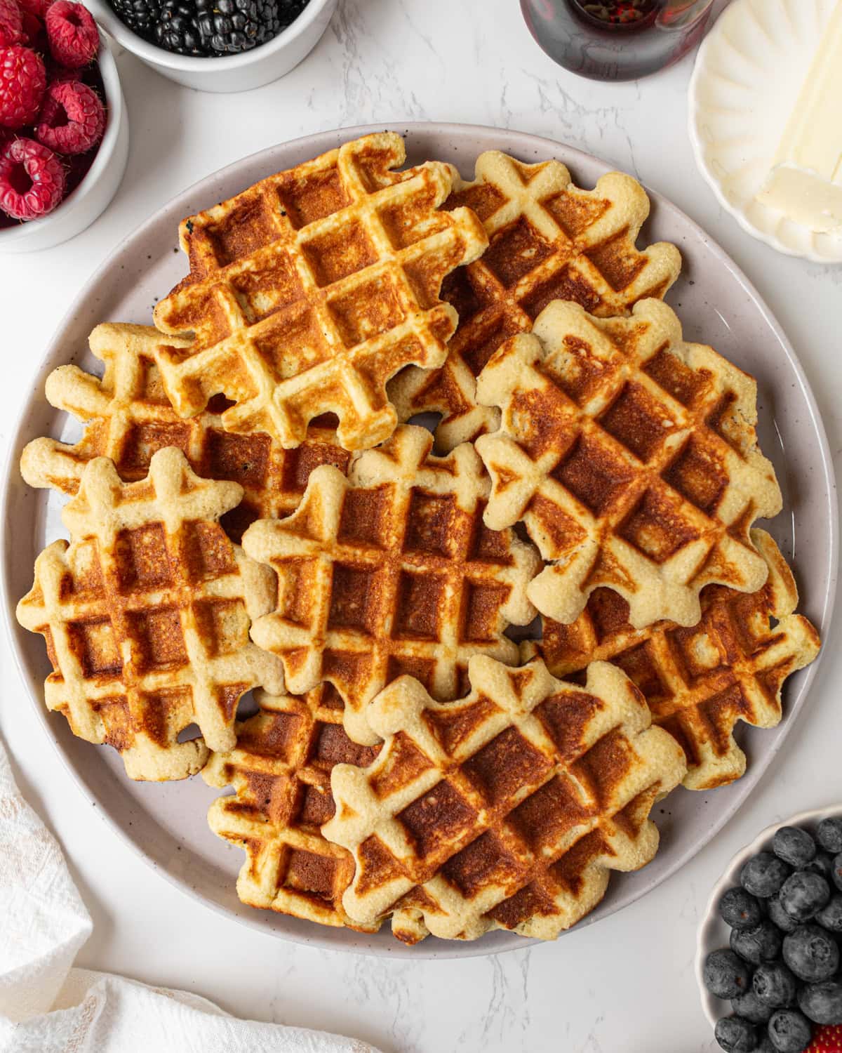 Plate of golden brown gluten-free coconut flour waffles served with fresh berries, butter, and maple syrup