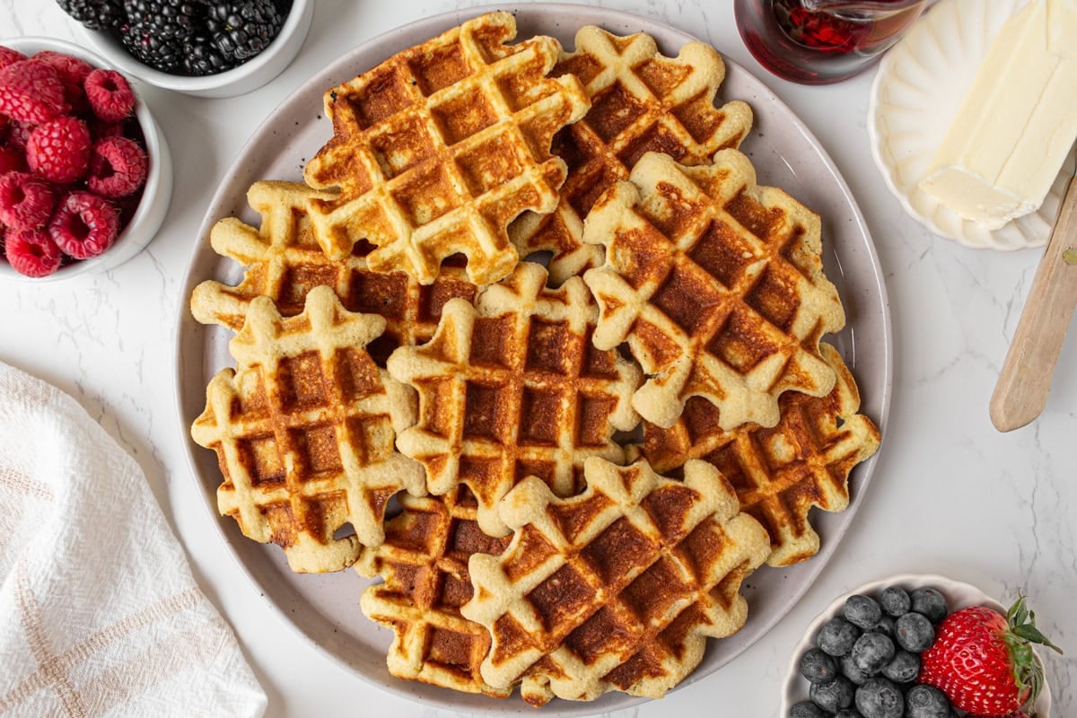 Overhead view of coconut flour waffles with raspberries, blackberries, blueberries, and butter on a plate