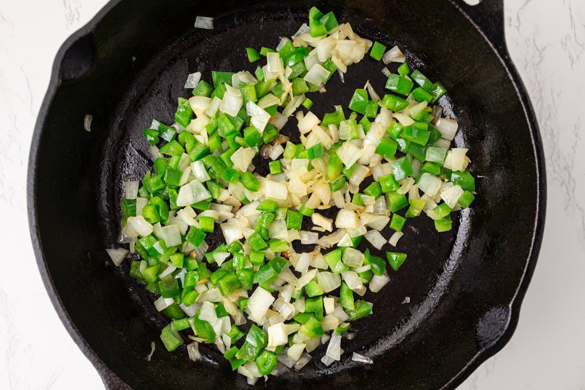 Diced green bell pepper and onion cooking in a cast iron skillet