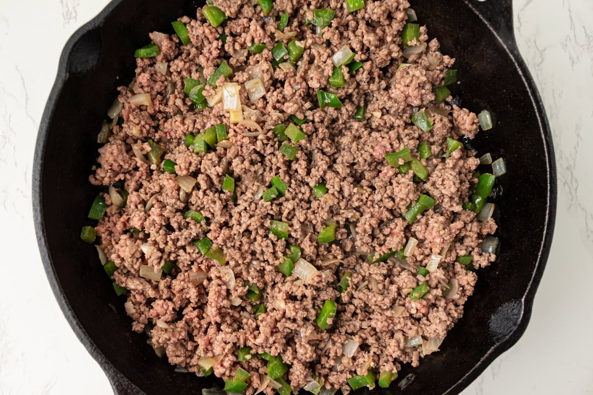 Ground beef cooking with softened peppers and onions in a skillet