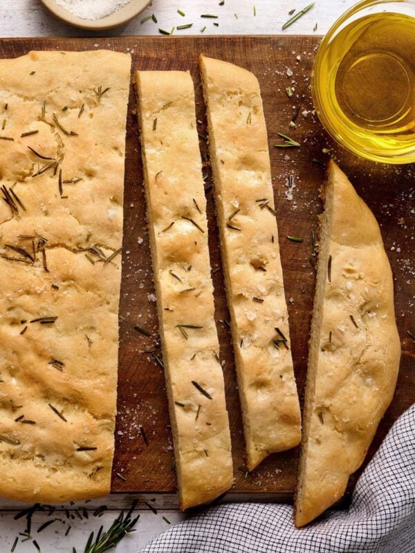 Sliced gluten-free focaccia bread with rosemary and flaky salt served on a wooden board with olive oil for dipping