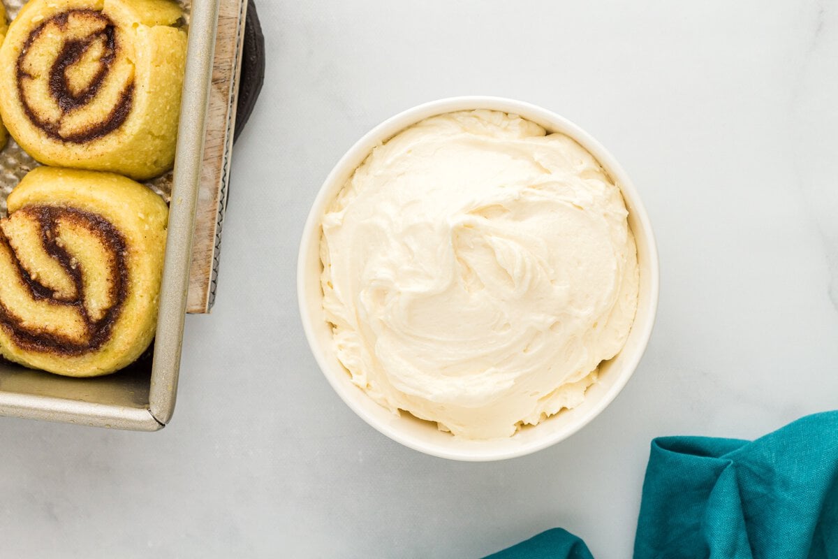 Cream cheese frosting in a bowl next to baked keto cinnamon rolls