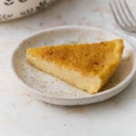 Slice of gluten-free crustless custard pie on a white plate with nutmeg sprinkled on top