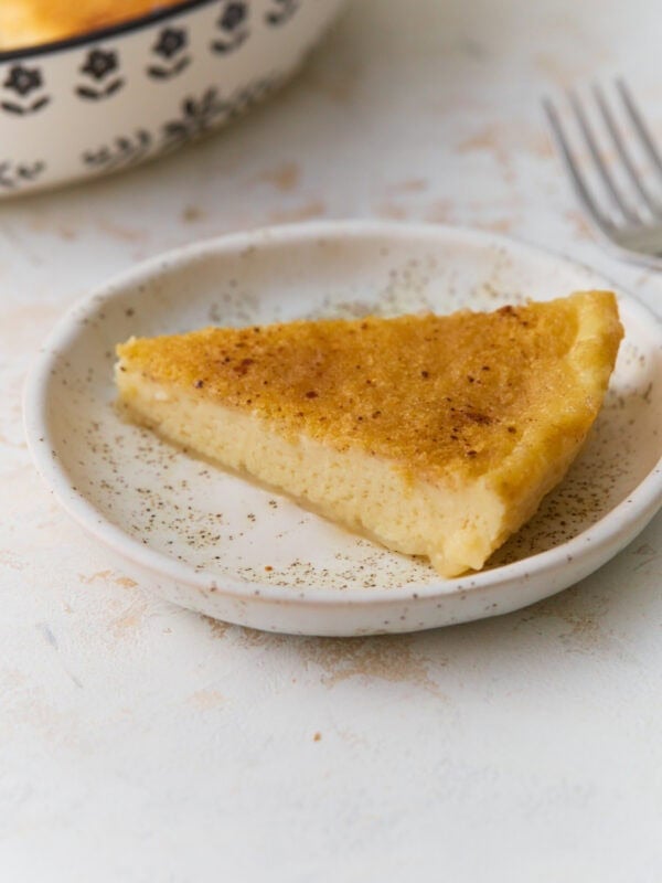 Slice of gluten-free crustless custard pie on a white plate with nutmeg sprinkled on top