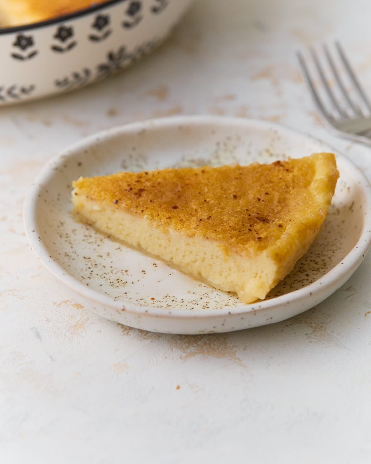Slice of gluten-free crustless custard pie on a white plate with nutmeg sprinkled on top