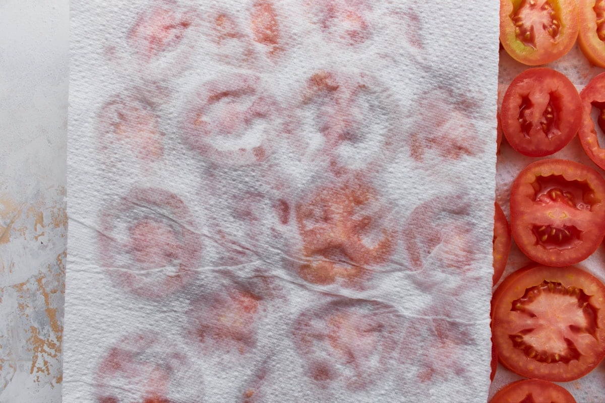 Paper towels pressed over sliced tomatoes to absorb excess moisture for crustless tomato pie.