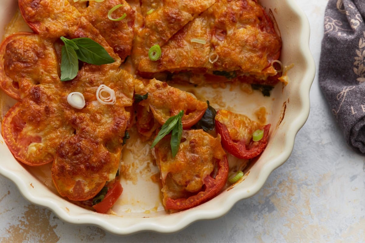 Crustless tomato pie sliced in a white baking dish with visible layers of tomatoes, basil, and melted cheese.