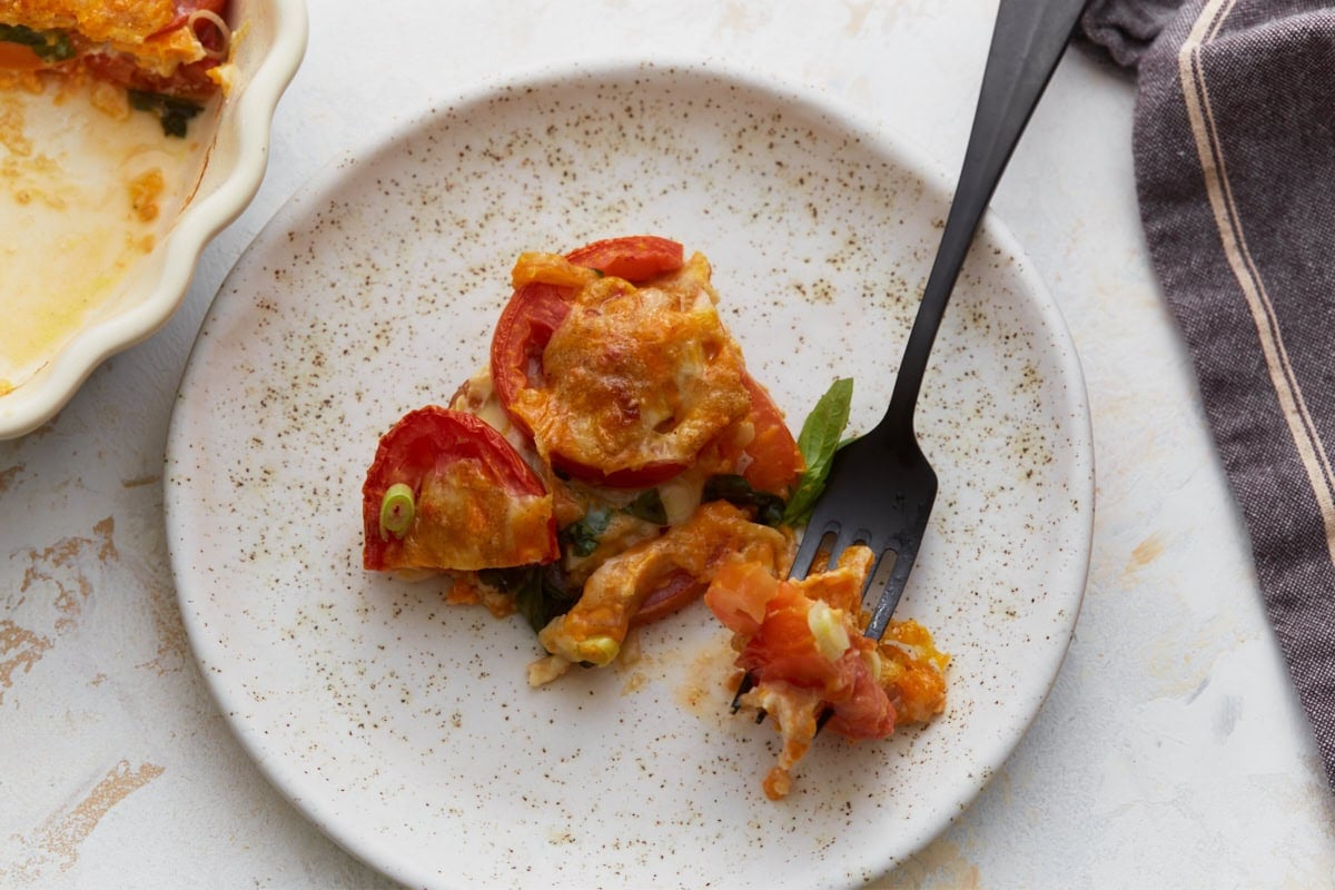 Slice of crustless tomato pie served on a plate with melted cheese, fresh tomatoes, basil, and green onions.
