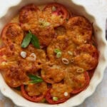 Overhead view of baked crustless tomato pie topped with melted cheese, fresh basil, and sliced green onions in a white pie dish.