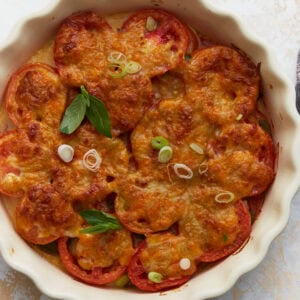 Overhead view of baked crustless tomato pie topped with melted cheese, fresh basil, and sliced green onions in a white pie dish.