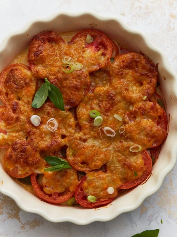 Overhead view of baked crustless tomato pie topped with melted cheese, fresh basil, and sliced green onions in a white pie dish.