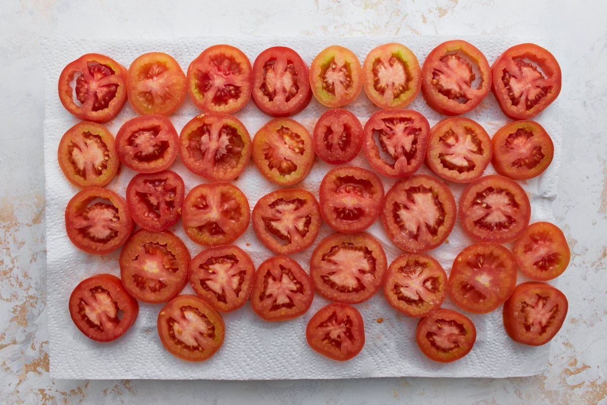 Sliced fresh tomatoes arranged on paper towels to drain excess moisture before making crustless tomato pie.