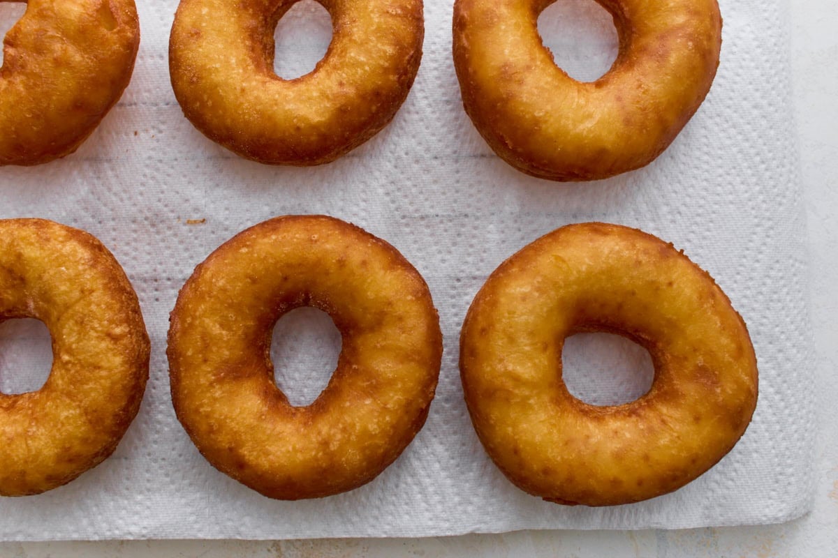 Freshly fried gluten-free mochi donuts cooling on paper towels before adding powdered sugar