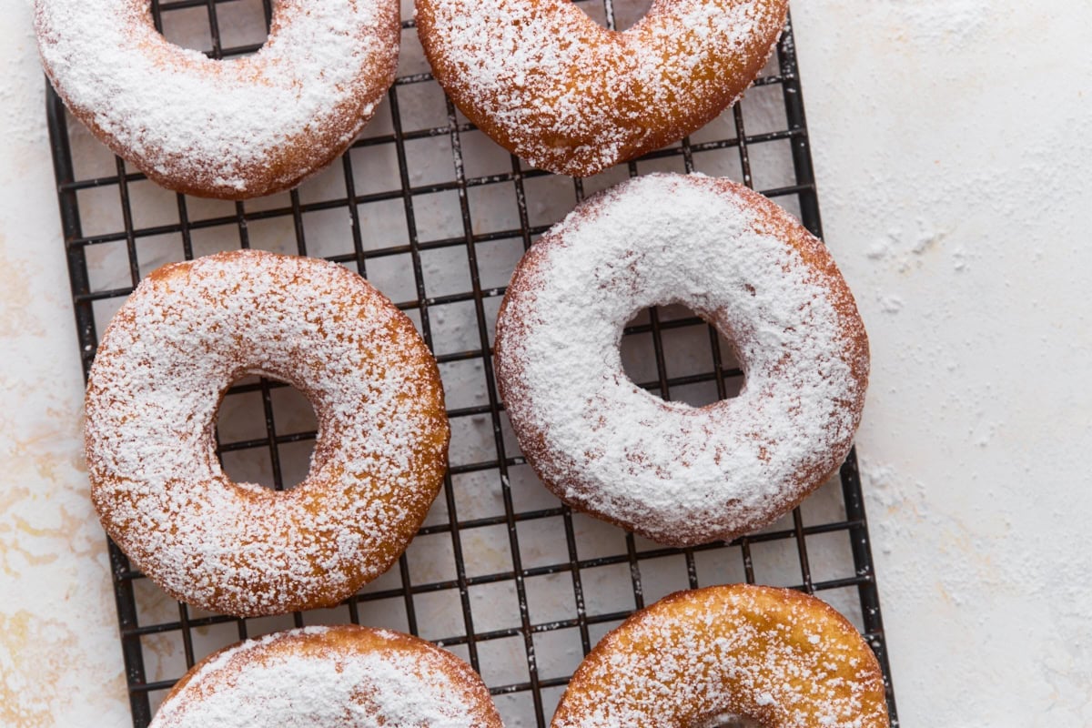 Freshly fried gluten-free mochi donuts dusted with powdered sugar on a cooling rack