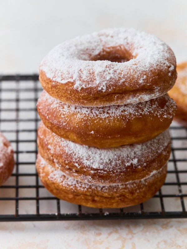 Stack of gluten-free mochi donuts dusted with powdered sugar on a cooling rack