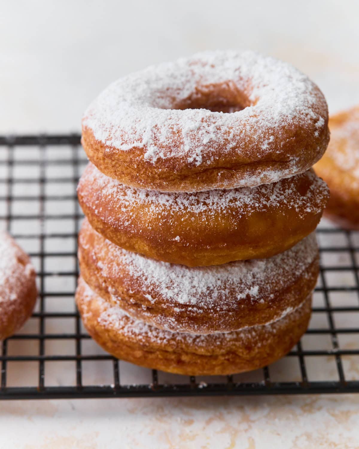 Stack of gluten-free mochi donuts dusted with powdered sugar on a cooling rack